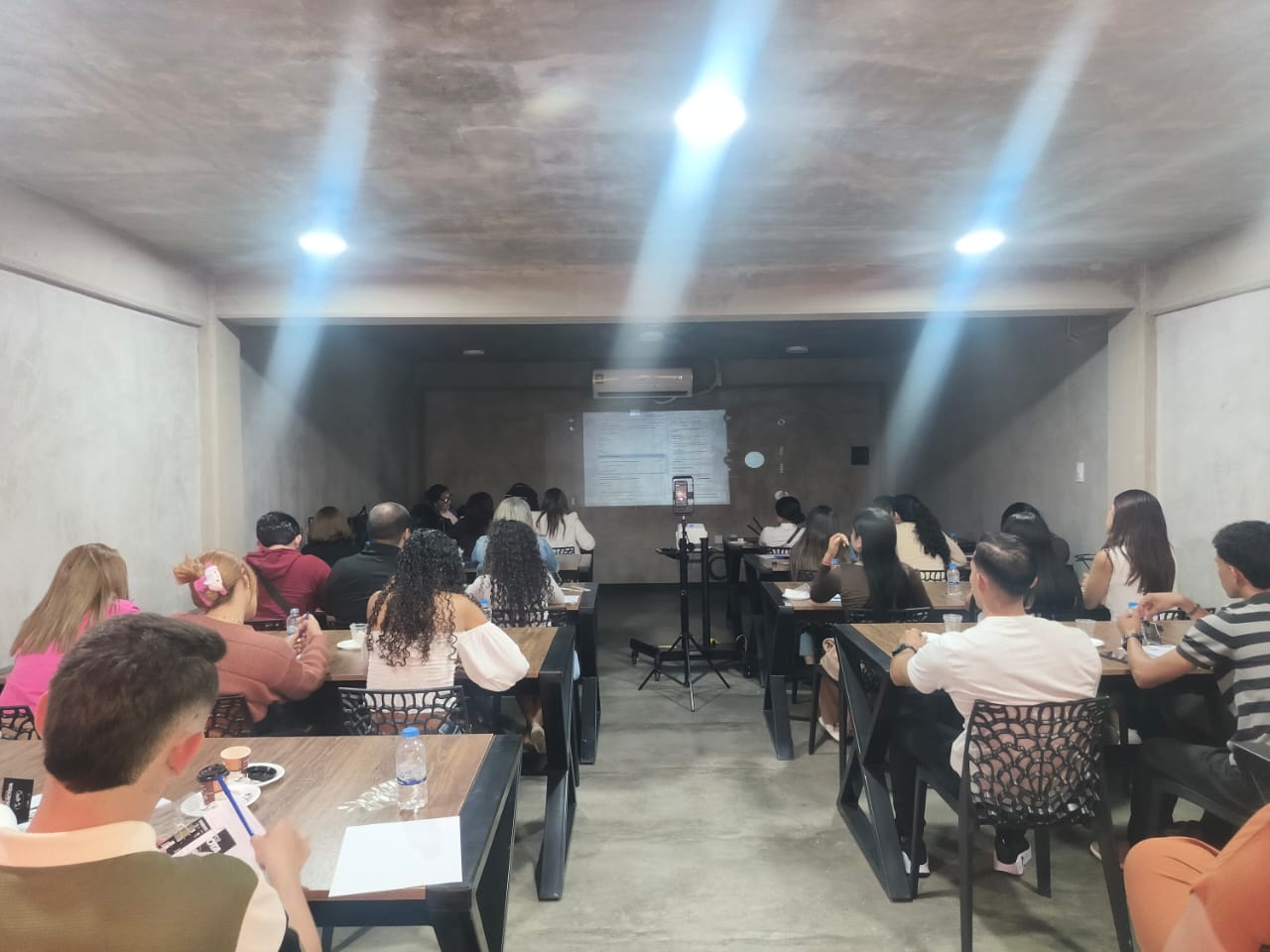 Salón lleno de participantes durante un curso con proyector encendido